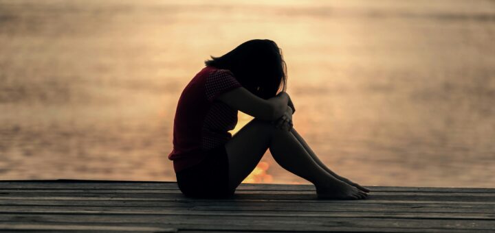 A woman sitting alone on a wooden dock by the lake, showing solitude and reflection.