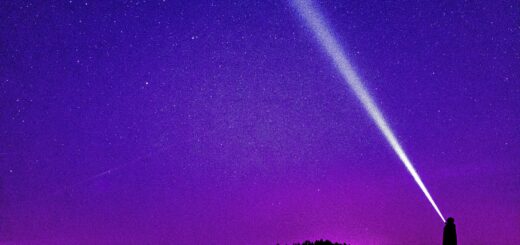 Silhouette of a person shining a flashlight under a starry violet night sky, creating a dramatic scene.