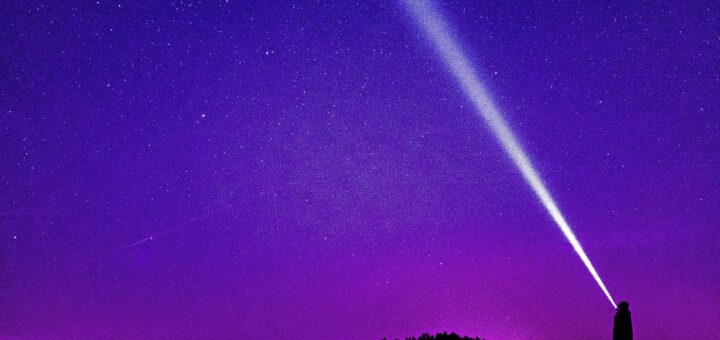 Silhouette of a person shining a flashlight under a starry violet night sky, creating a dramatic scene.