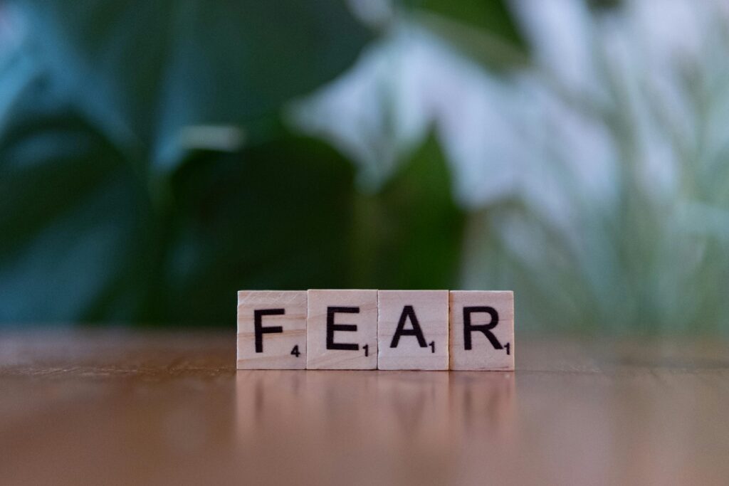 Wooden letter blocks spelling 'FEAR' on table against blurred green background. Emphasizes emotion and challenge.