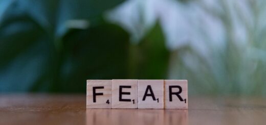 Wooden letter blocks spelling 'FEAR' on table against blurred green background. Emphasizes emotion and challenge.