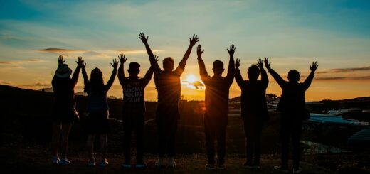 A diverse group of friends raises their arms in celebration against a vibrant sunset backdrop.