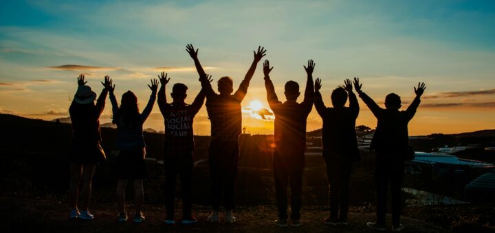 A diverse group of friends raises their arms in celebration against a vibrant sunset backdrop.