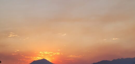 Sunrise glowing behind mountain silhouettes in Utah, with orange and pink skies softened by wildfire haze.